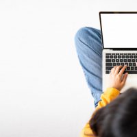 Top view of woman sitting on floor and using laptop blank screen white background. Mockup, template for your text, Clipping paths included for device screen. Panoramic image with empty copy space